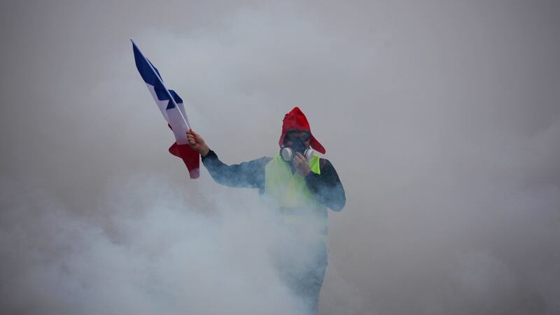 A demonstrator holds up  a furled French flag  amid billowing tear gas during a “gilets jaunes” (yellow vests) protest against rising oil prices and living costs in Paris. Photograph: AFP/Getty Images