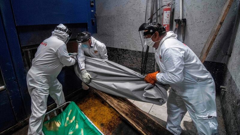 Employees put a body bag with the remains of a victim of Covid-19 in an oven at a crematorium in Mexico City. Photograph:  Pedro Pardo/AFP via Getty Images