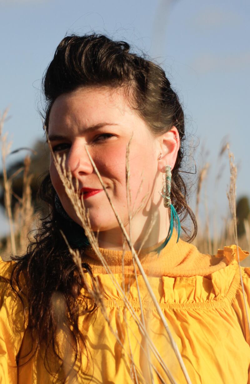 Head and shoulders shot of Clare Sands, wearing a yellow dress, with head turned to left, and standing in a field of corn