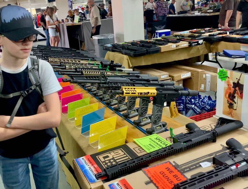 A young boy examines a gun display at the Tuscon gun show. Note the 
weapon with the name Trump on the pistol grip and handguard, which was selling for $1,195.