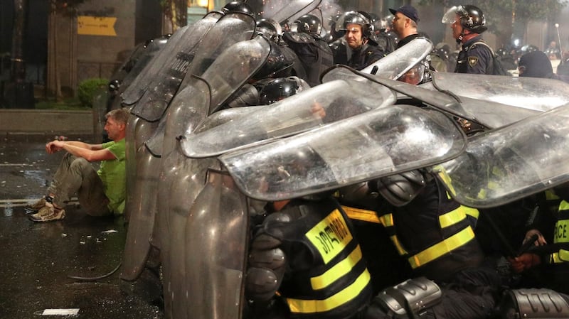 A protester sits on the ground next to riot policemen  near the Georgian parliament in Tbilisi. Photograph:  Irakli Gedenidze/Reuters