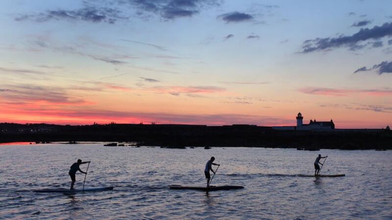 Dan King, Dan Gardner and Joseph Gallagher pass by Mutton Island lighthouse on their stand-up paddleboards on  Saturday night.  Photograph: Joe O’Shaughnessy