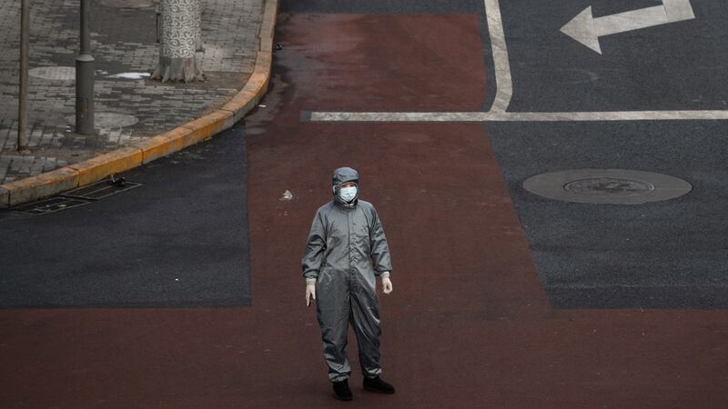 A Chinese woman wears a protective suit and mask as she waits to cross the intersection of a nearly empty street on February 8th  in Beijing, China. Photograph: Kevin Frayer/Getty