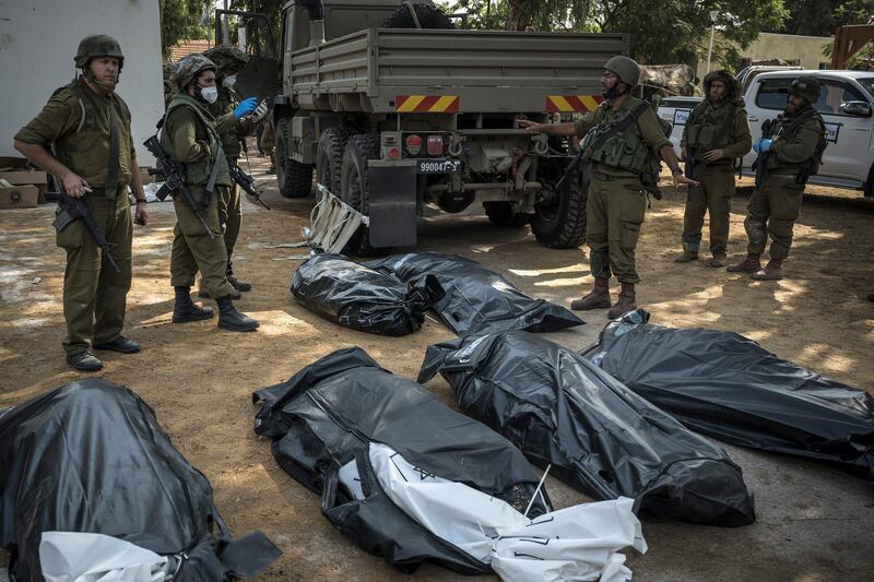 Israeli soldiers check the bodies of people killed in Kfar Azza, a village just across the border from Gaza that was attacked by Palestinian gunmen at the weekend. Photograph: Sergey Ponomarev/New York Times
                      