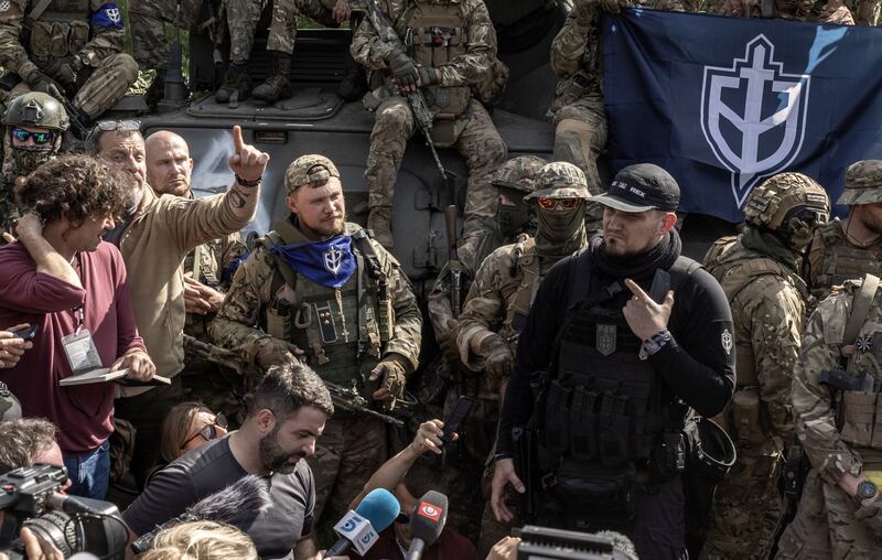 Denis Kapustin, in black,  is interviewed and photographed by reporters in the northeastern Ukraine in May 2023. The RDK founder has been a prominent figure in Russian and German football hooligan and far-right mixed martial arts communities. Photograph: Finbarr O’Reilly/New York Times
                      