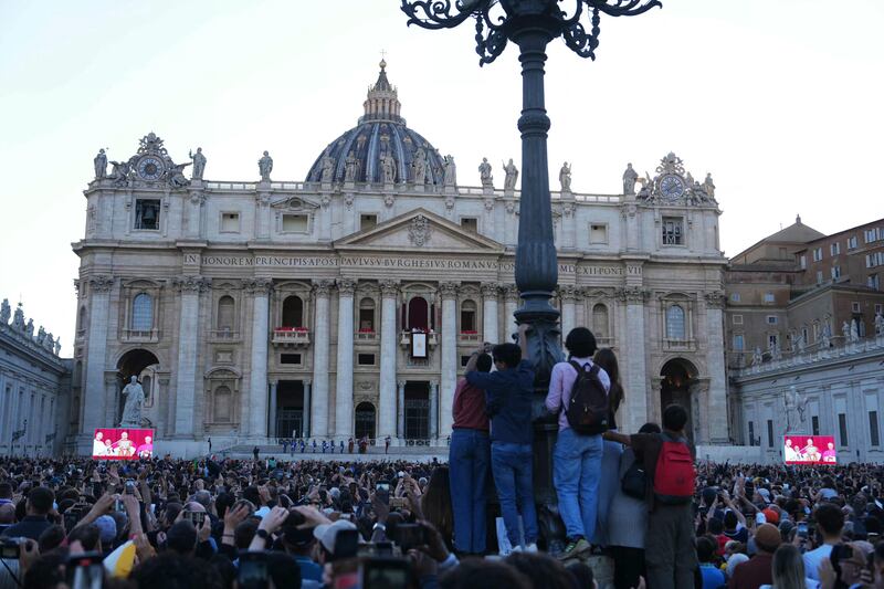 People listen to newly elected Pope Robert Francis Prevost, Pope Leo XIV, addressing the crowd from the main central loggia balcony of the St Peter's Basilica for the first time. Photo by Dimitar DILKOFF / AFP