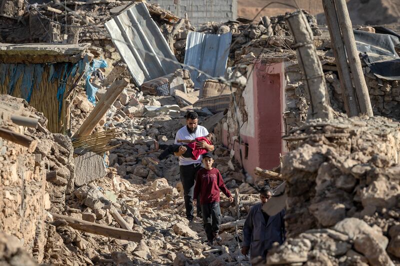 A man carries his young child as he picks his way through the rubble of his village which has been completely destroyed by the earthquake. © UNICEF/Morocco,2023/Senna/AFP -