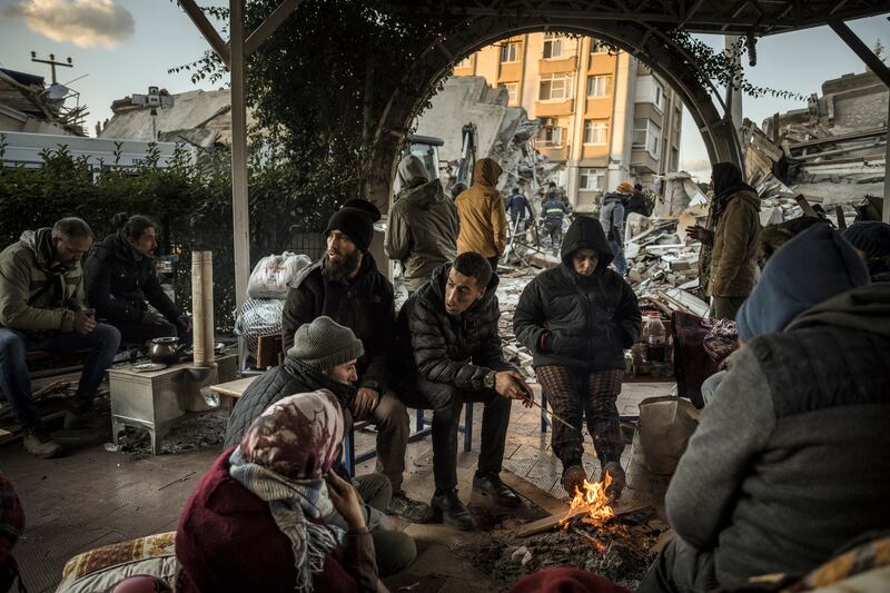 A family warms themselves around a fire near a collapsed building in Antakya, Turkey. Photograph: Sergey Ponomarev/The New York Times