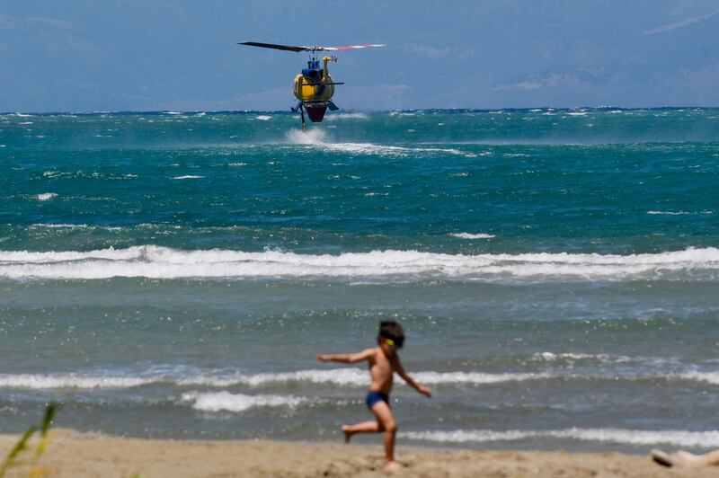 A boy plays on the beachfront as a firefighting helicopter hovers above the sea to refill water for a drop on wildfires near the village of Loutses on the Greek island of Corfu. Photograph:  Armend Nimani/AFP via Getty Images
