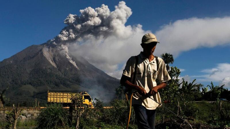 A farmer sprays pesticide as Mount Sinabung spews ash into the air at Sibintun village in Karo district, Indonesia’s North Sumatra province. Photograph: Beawiharta/Reuters