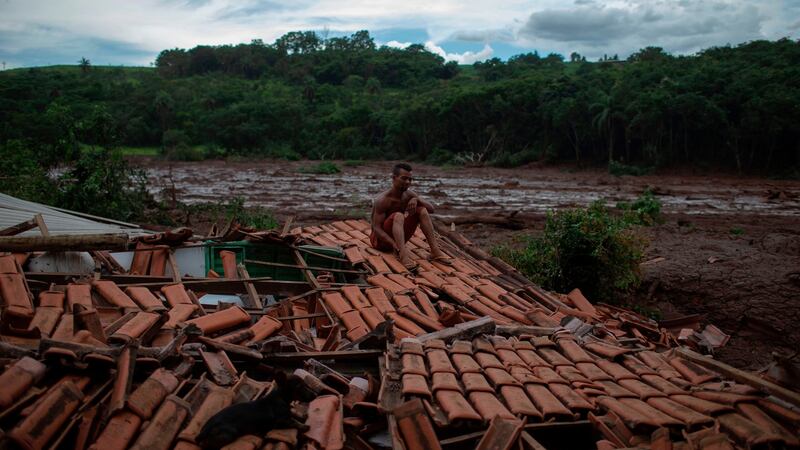 ‘Everything was shaking and I saw huge trees and people disappearing under the mud,’ said Emerson dos Santos, 30, who sits on the roof of his family home to protect what is left from looters at the mud-hit area a day after the  dam collapse. Photograph:  Mauro Pimentel/AFP/Getty Images