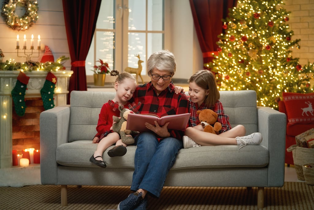 Grandmother reading a book to her grand daughters near Christmas tree.
