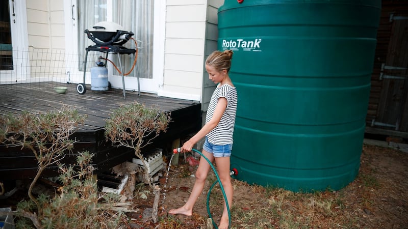 A  girl waters a plant from a rainwater storage tank in Cape Town, South Africa. Watering plants using municipal water has been banned in the city. When  dam levels reach 13.5 per cent, most taps will be turned off. Photograph: Nic Bothma/EPA