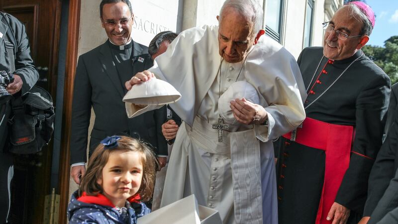 Pope Francis (C) accompanied by Leiria-Fatima Bishop Antonio Marto (R) changes skull-caps with a young child at the entrance of the Our Lady Rosario Cathedral at the Fatima Sanctuary. Photograph: Paulo Cunha/ EPA
