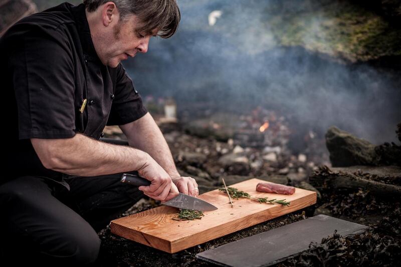 William McElhinney preparing food in an outdoor  firepit