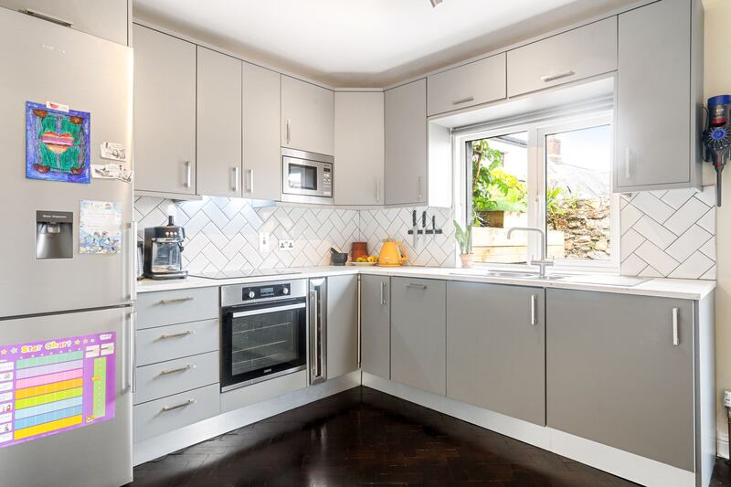 The modern kitchen is accessed through an alcove; it has light-grey units and a white-tile splashback in a herringbone pattern.