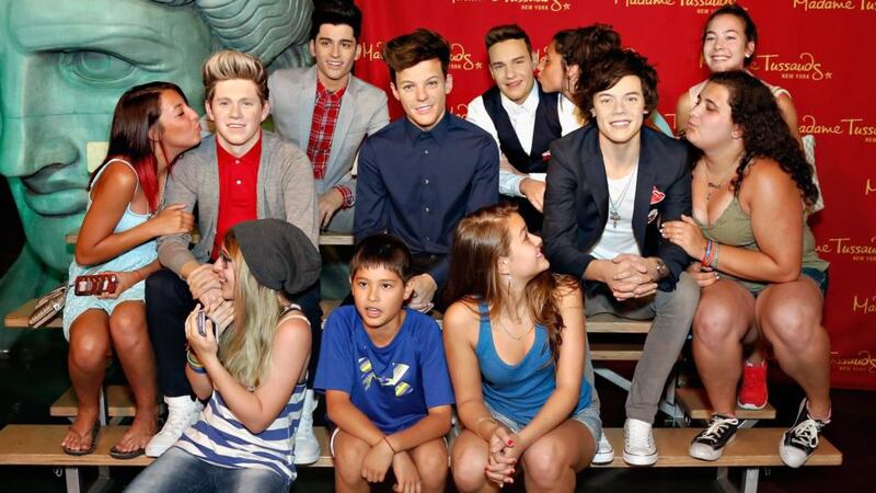 Fans pose with the wax figures of  One Direction.  Photograph: Getty