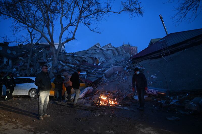 People seek warmth by a bonfire bonfire amid collapsed buildings in Kahramanmaras, Photograph: Ozan Kose//AFP via Getty Images