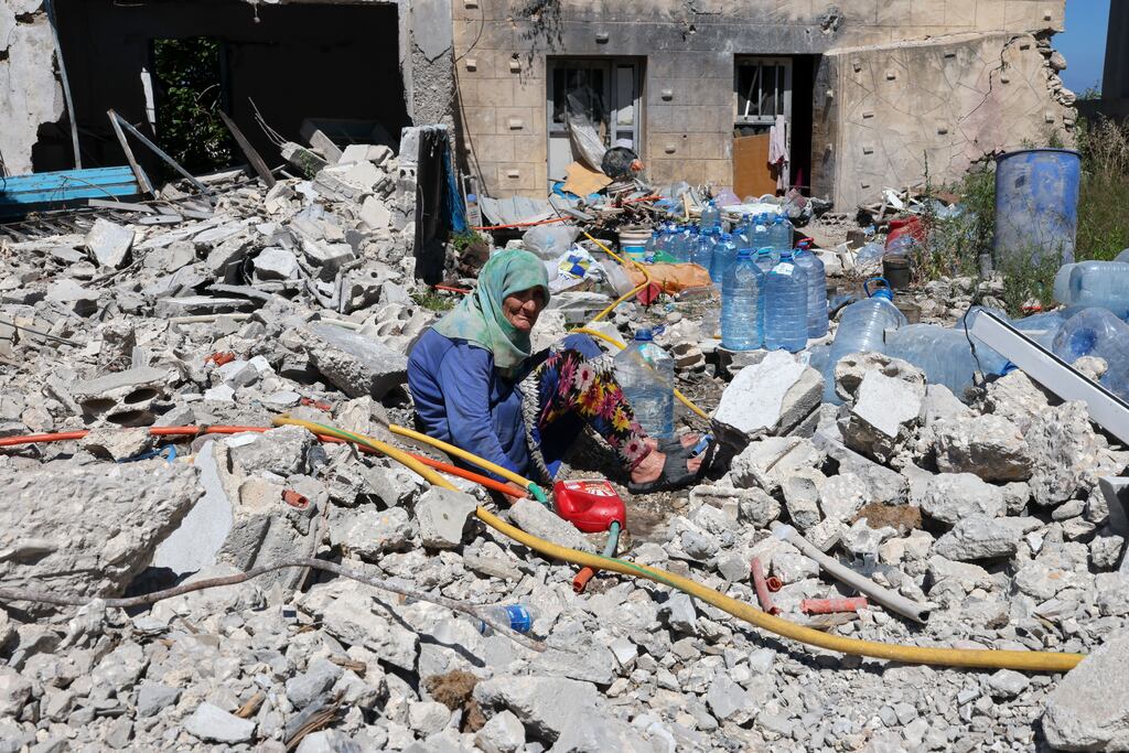 Khadija Amara, an elderly woman, fills a jerrycan with water as she sits amid the rubble of her house damaged by an Israeli strike in the village of Qlaileh, southern Lebanon. Photograph: EPA
